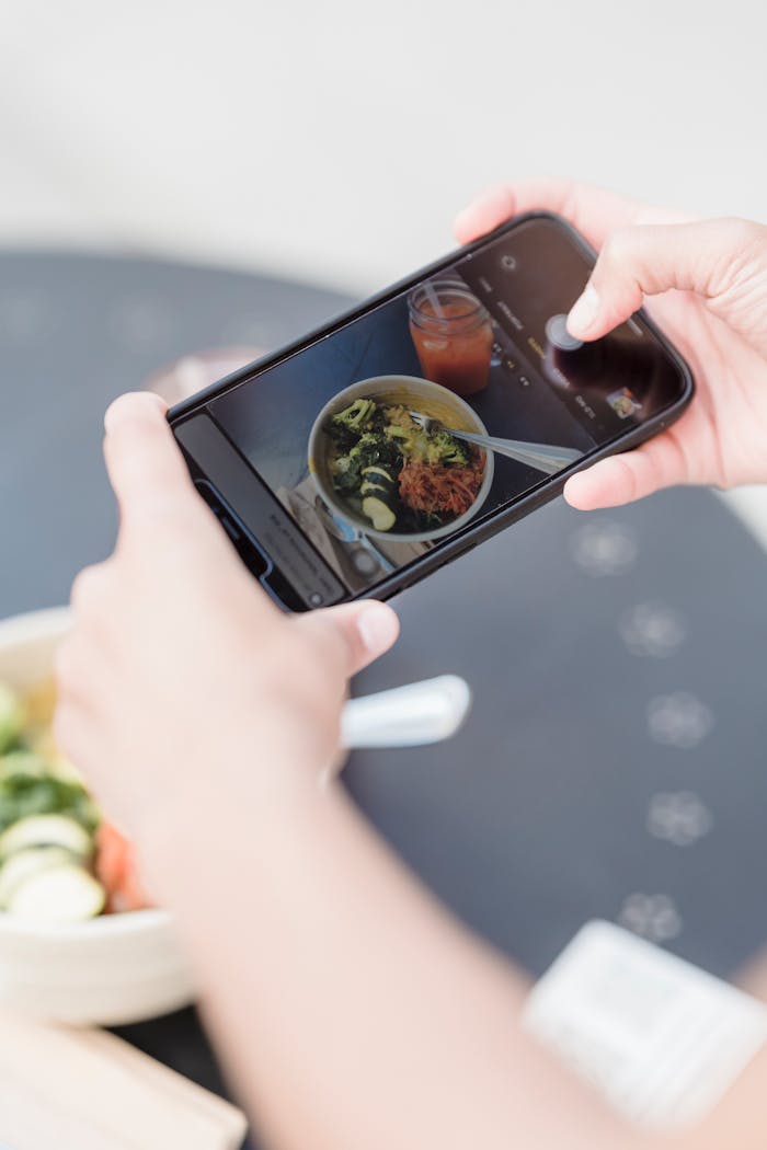 From above of crop unrecognizable blogger taking photo of vegetarian salad and smoothie on cellphone in street cafe