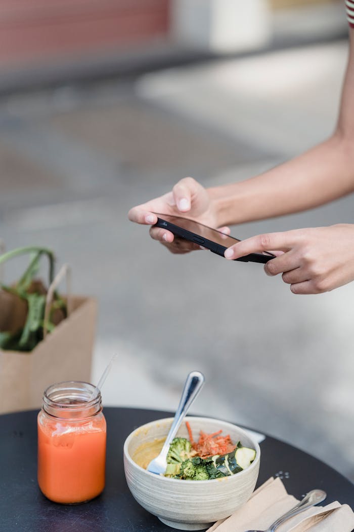 contact-img Crop anonymous female blogger taking photo of healthy lunch and smoothie on mobile phone above street cafe table