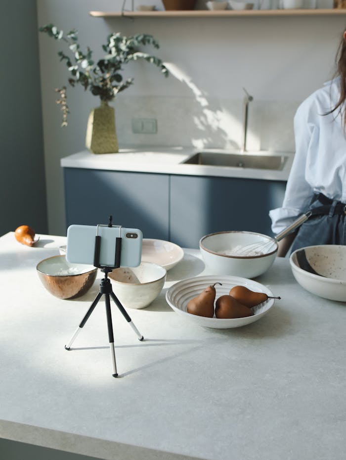 A modern kitchen countertop organized with ceramic bowls and a mobile setup for food blogging.