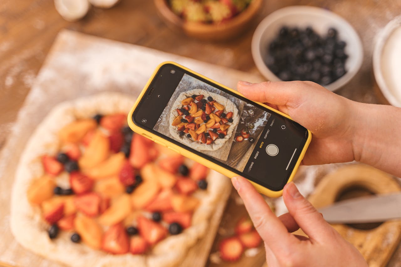 Person taking a photo of a homemade fruit pie with a smartphone.